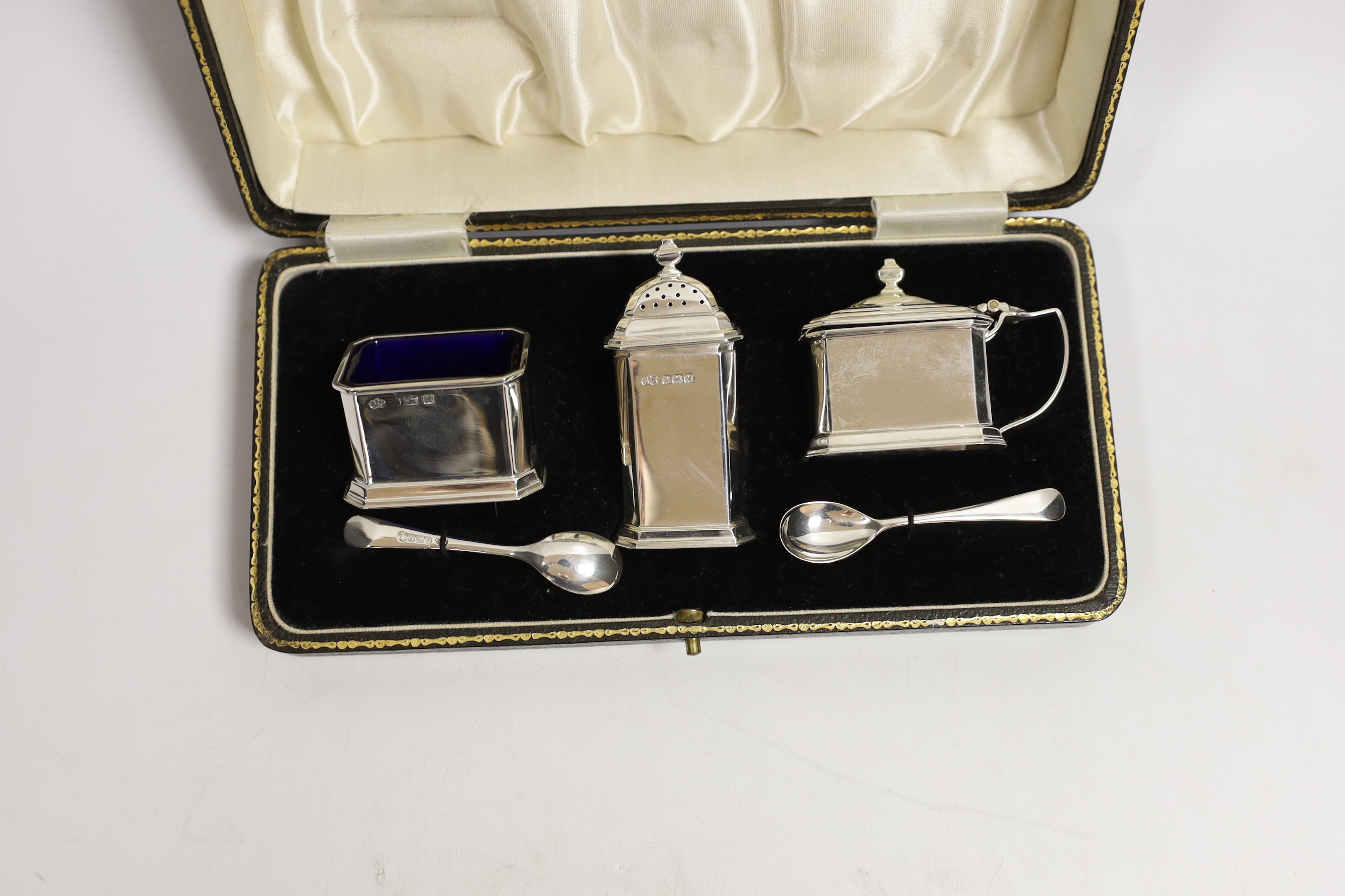 A cased George VI silver three piece condiment set, Elkington & Co, Birmingham, 1936 and two spoons, one matching silver, the other plated replacement.